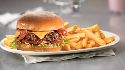 A juicy cheeseburger with bacon, lettuce, and tomato, served with a side of golden French fries on a plate.