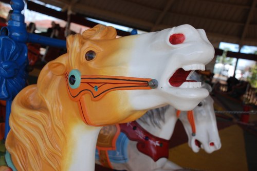 Close-up of a colorful carousel horse with a painted mane and detailed features, set in a vibrant amusement park.