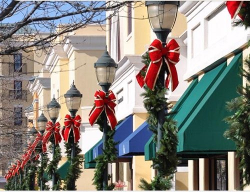 Decorated street with festive red bows and greenery on lamp posts, set against a backdrop of colorful storefronts.