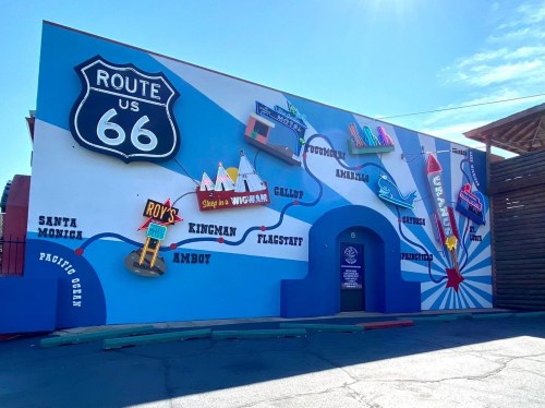 Colorful mural depicting Route 66 with city names and landmarks, set against a bright blue sky.