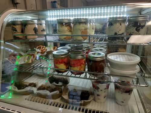 A display case filled with various desserts in jars, including fruit, yogurt, and chocolate treats.