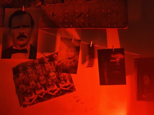A collection of vintage black-and-white photos hanging on a string, illuminated by red light.