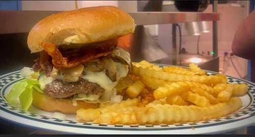 A juicy burger topped with bacon, cheese, and lettuce, served with a side of crinkle-cut fries on a checkered plate.