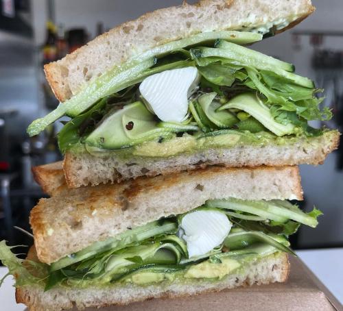 A close-up of a sandwich with layers of green vegetables, including lettuce and cucumber, on whole grain bread.