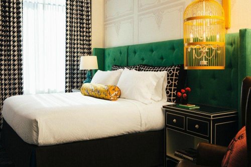 Cozy hotel room featuring a green upholstered headboard, white bedding, and stylish decor with a lamp and side table.