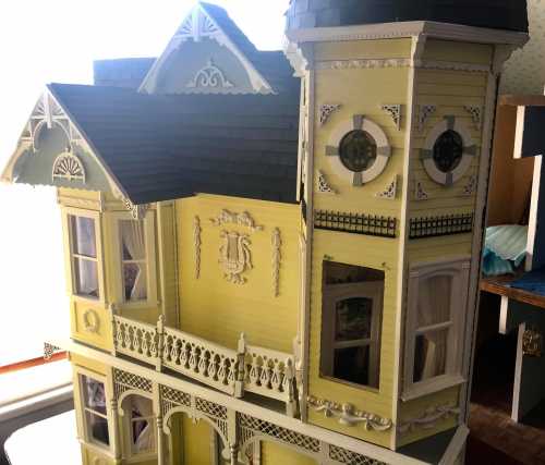 A detailed yellow dollhouse with intricate architectural features and a tower, set against a bright window.