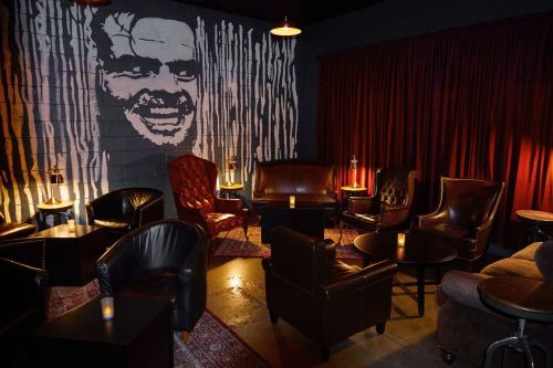 Cozy lounge with leather chairs, dim lighting, and a large mural of a smiling face on the wall.
