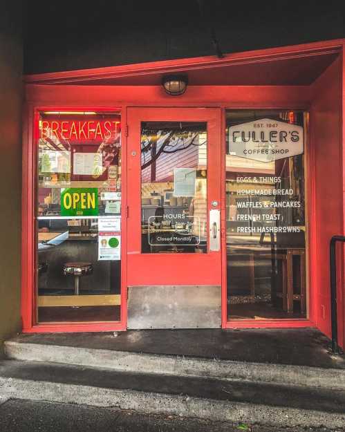 A cozy coffee shop entrance with a bright red door, featuring a "Breakfast" sign and an "Open" indicator.