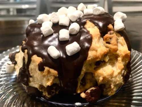 A large dessert topped with chocolate glaze and mini marshmallows, sitting on a glass plate.