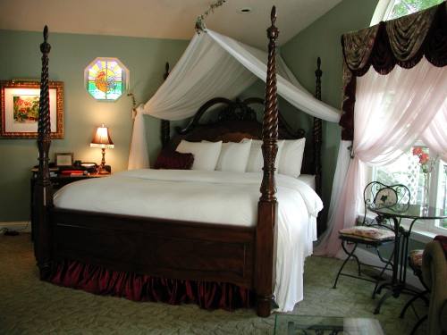 A cozy bedroom featuring a four-poster bed with white linens, elegant drapes, and a small seating area by a window.