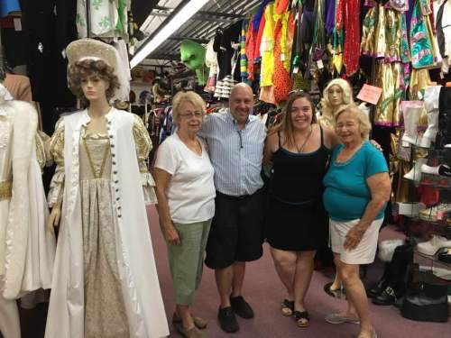 A group of four people poses together in a colorful costume shop filled with various outfits and accessories.