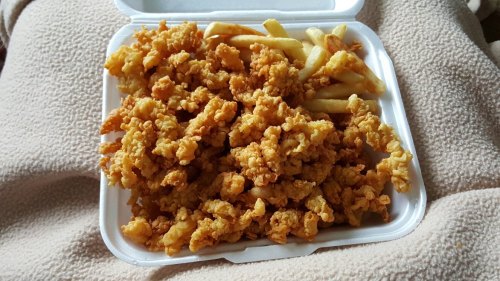 A takeout container filled with crispy fried chicken pieces and a side of French fries.