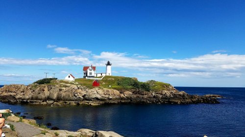 A scenic view of a lighthouse on a rocky island, surrounded by calm blue waters and a clear sky.