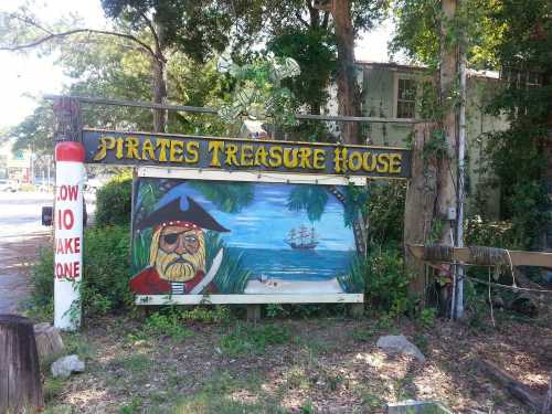 Sign for "Pirates Treasure House" featuring a pirate and a ship in the background, surrounded by trees.