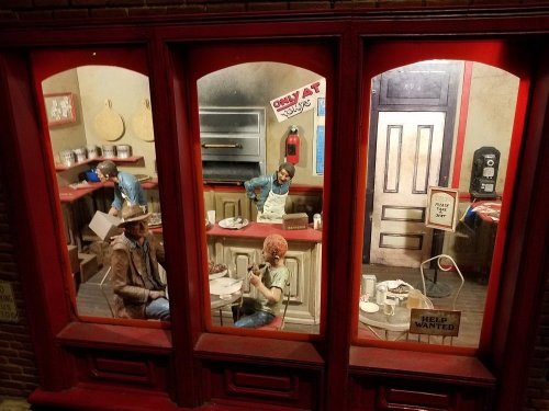 A detailed diorama of a diner scene with figures seated at tables and a counter, showcasing a nostalgic atmosphere.