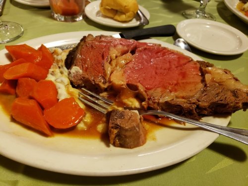 A plate of prime rib with carrots and mashed potatoes, garnished with gravy, on a green tablecloth.