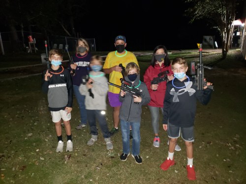 A group of children wearing masks and holding toy guns, standing together outdoors at night with glow sticks.
