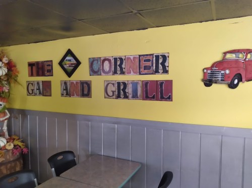 Interior of a restaurant with a yellow wall displaying "The Corner Gas and Grill" sign and a vintage red truck decoration.