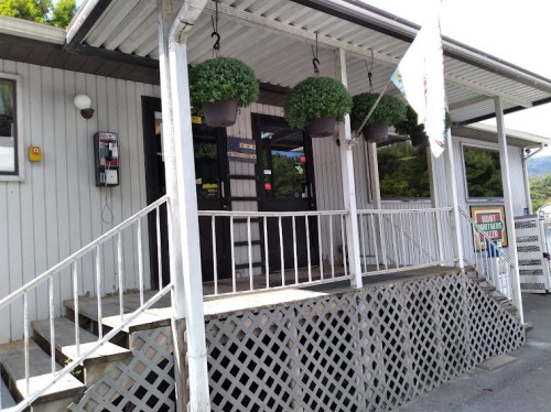 A small building entrance with potted plants hanging, a payphone, and a sign on the side. Steps lead up to the door.