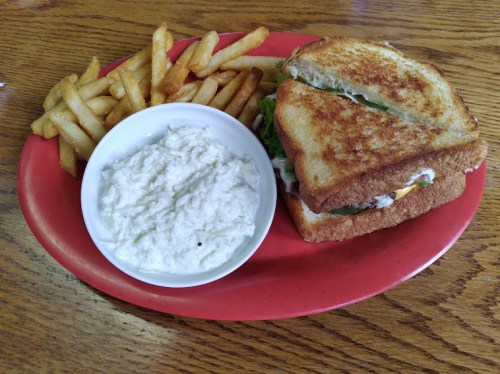 A plate with a grilled sandwich, a side of fries, and a bowl of creamy dip on a wooden table.