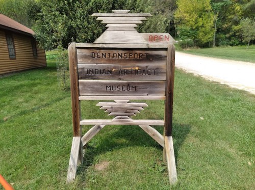 Sign for Bentonsport Indian Artifact Museum, with "OPEN" displayed, surrounded by greenery and a dirt path.