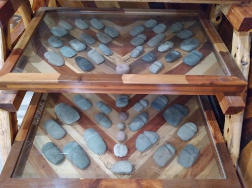 Two glass display cases containing various smooth stones arranged on a wooden base with a chevron pattern.