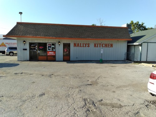 Exterior of Nally's Kitchen, a small restaurant with a sign, parking lot, and clear blue sky.