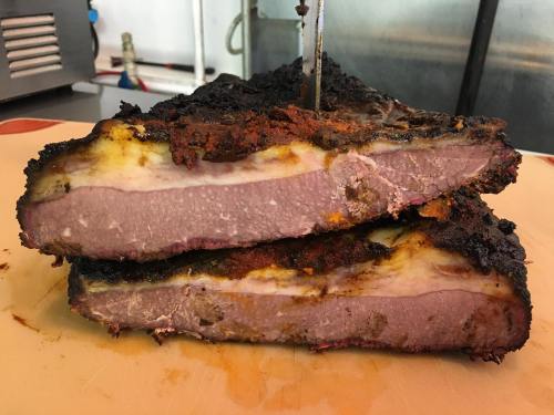 Close-up of two thick slices of smoked brisket with a charred crust and visible layers of meat and fat.