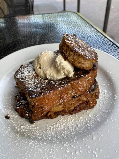 A plate of French toast topped with whipped cream and a slice of cake, dusted with powdered sugar.