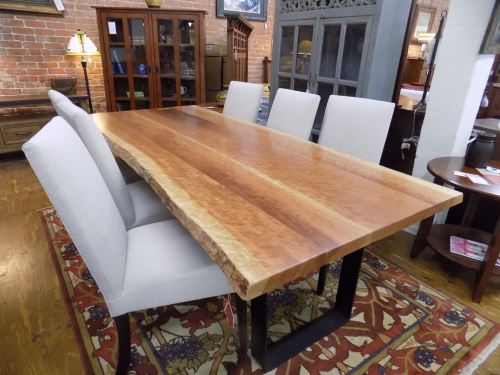 A rustic wooden dining table with a live edge, surrounded by four upholstered chairs in a cozy interior setting.