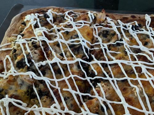 A close-up of a pizza topped with cheese, vegetables, and drizzled with mayonnaise.