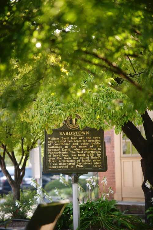 A historical marker for Bardstown, partially obscured by green leaves, detailing its founding and history.