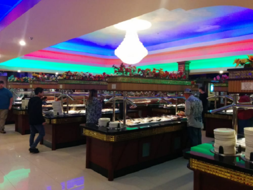A vibrant buffet restaurant with colorful lighting and diners serving themselves from various food stations.