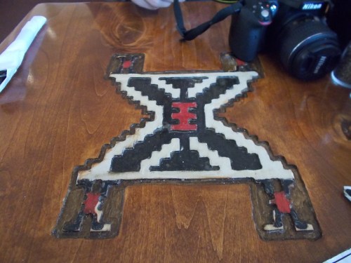 A wooden table with a colorful geometric design featuring black, red, and cream colors. A camera is nearby.