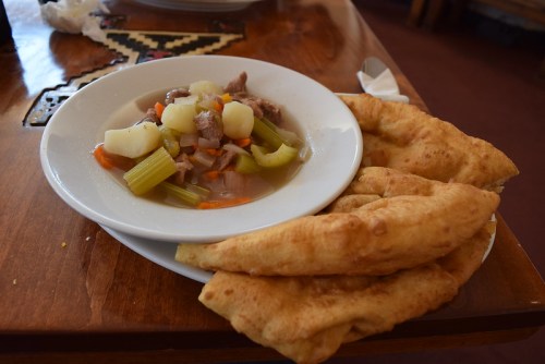 A plate of hearty meat and vegetable stew with potatoes, served alongside two pieces of golden-brown flatbread.