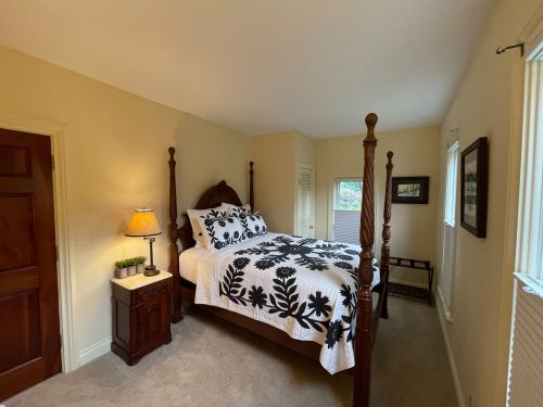 Cozy bedroom featuring a four-poster bed with a black and white floral quilt, nightstand, and natural light from windows.