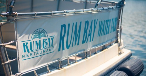 Sign on a boat displaying "Rum Bay Restaurant" and "Rum Bay Water Taxi" against a water background.