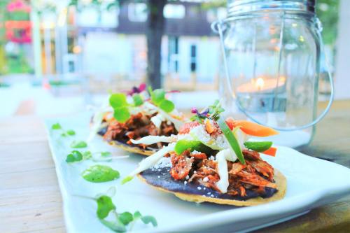 Two tacos topped with shredded meat, vegetables, and sauce, served on a white plate with a lantern in the background.