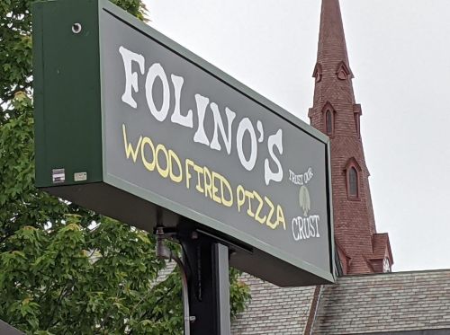 Sign for Folino's Wood Fired Pizza, featuring a green background and a church steeple in the background.