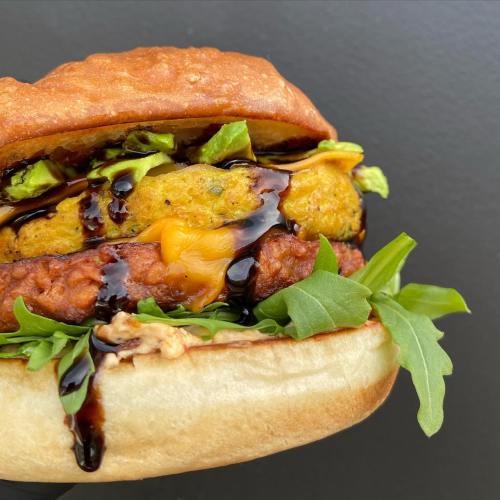 A close-up of a sandwich with crispy chicken, cheese, lettuce, and a drizzle of sauce on a toasted bun.