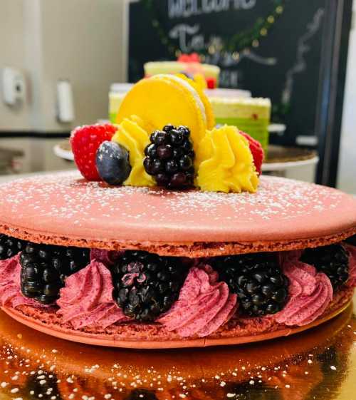 A large pink macaron filled with blackberries and raspberry cream, topped with yellow and red fruit garnishes.