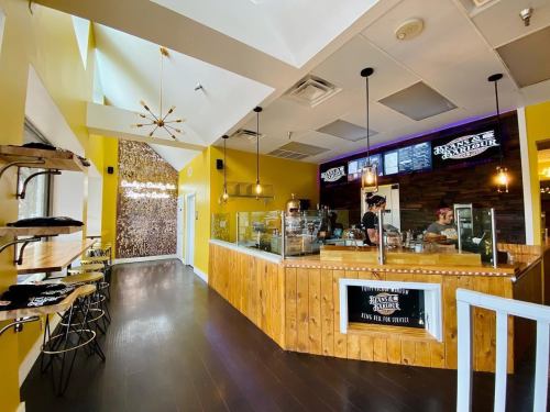 Brightly lit café interior with yellow walls, wooden counter, and a barista behind the counter. Modern decor and seating.