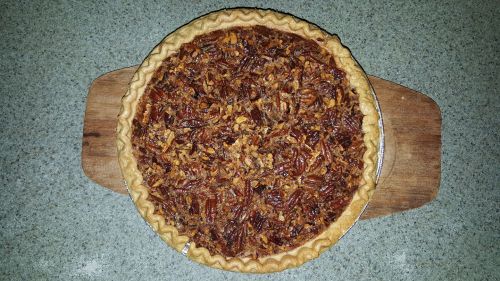 A freshly baked pecan pie on a wooden cutting board, with a golden crust and a rich, nutty filling.