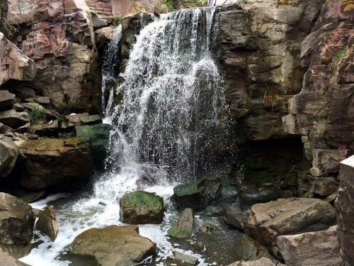 A cascading waterfall flows over rocky cliffs into a pool, surrounded by moss-covered stones.