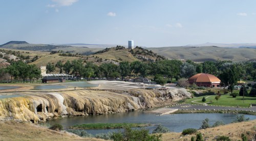 A scenic view of rolling hills, a river, and unique rock formations, with buildings and trees in the foreground.