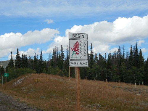 Sign marking the beginning of the Snowy Range Byway in Wyoming, surrounded by trees and open grassland.