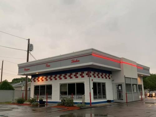 A retro-style fast food restaurant with a red and white exterior, featuring neon lights and a cloudy sky.