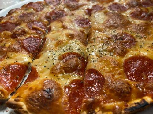Close-up of a pepperoni pizza with melted cheese and herbs, featuring a crispy crust and golden-brown toppings.