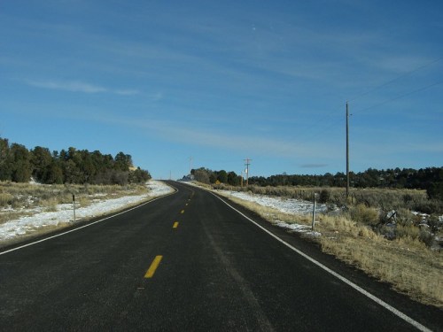 A winding road stretches into the distance, flanked by sparse vegetation and a clear blue sky.