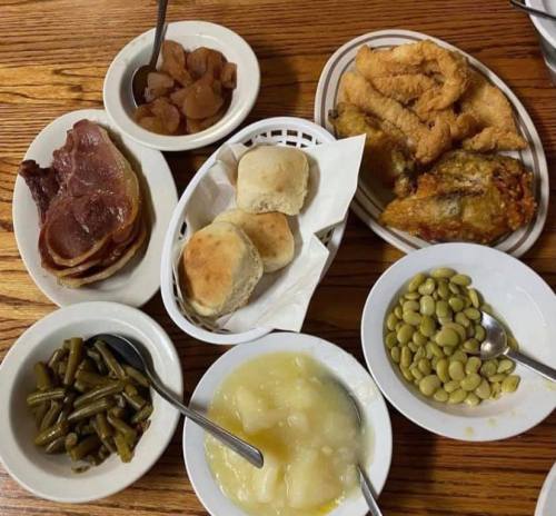 A spread of Southern comfort food including fried chicken, ham, biscuits, green beans, lima beans, and peach preserves.